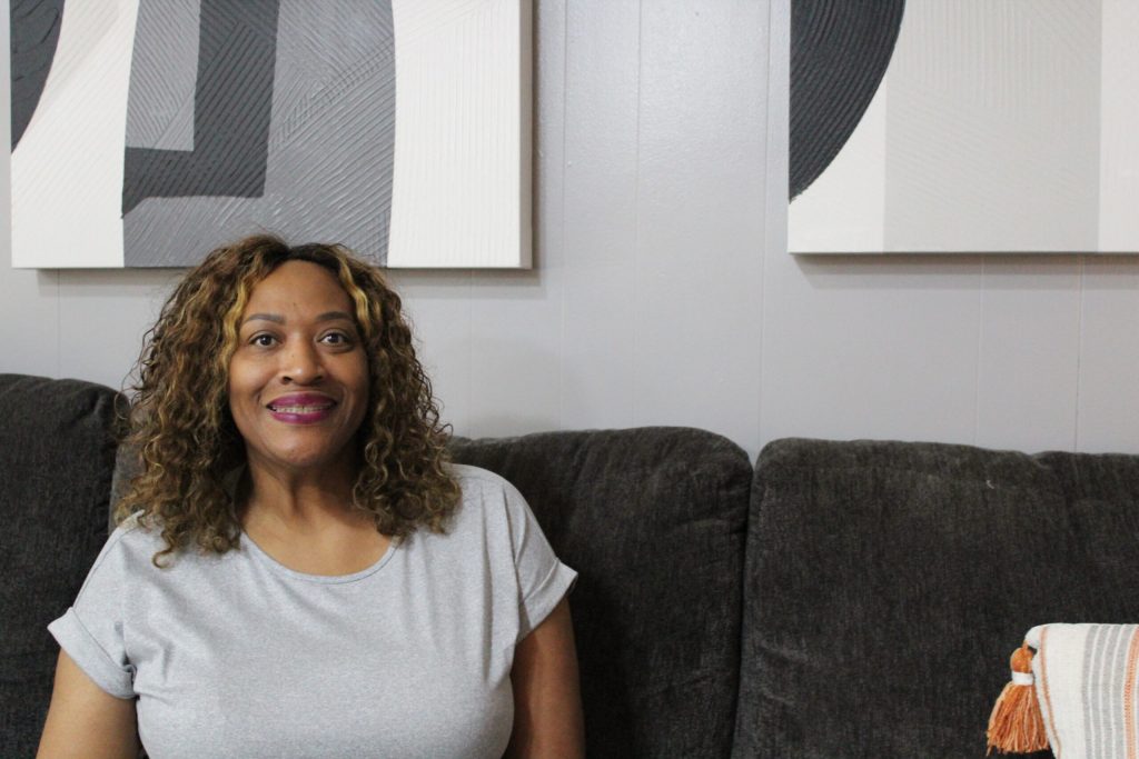 Woman of color sits on couch smiling at camera
