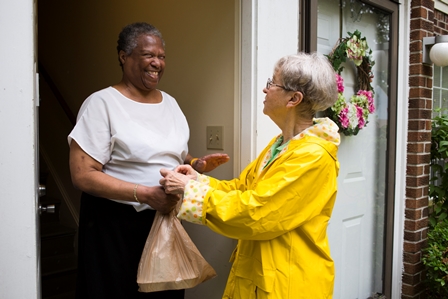 woman hands brown bag to woman standing in doorway